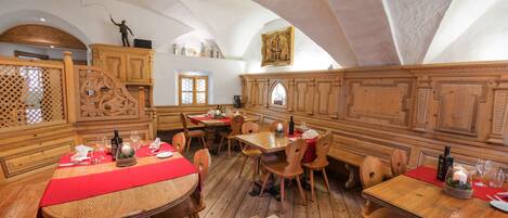 Interior de madera tradicional con techos altos y ventanas arqueadas. Mesas con manteles rojos y velas.