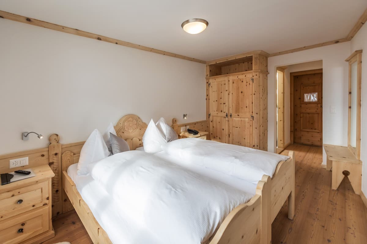 Una cama de madera con ropa de cama blanca, una mesita de noche con un control remoto y un armario de madera en una habitación con suelo y paredes de madera.