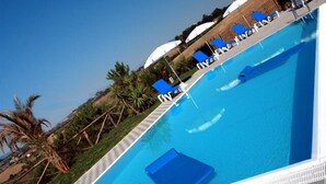 Une piscine à l’eau bleue, entourée de chaises longues et de parasols.