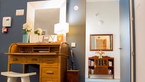 Una habitación con un escritorio de madera, una silla blanca, un espejo, una estantería y una puerta.