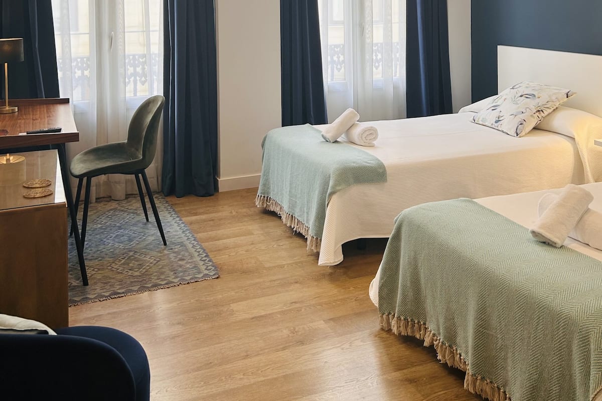 Une chambre d’hôtel avec deux lits, un bureau, une chaise et de grandes fenêtres avec des rideaux.