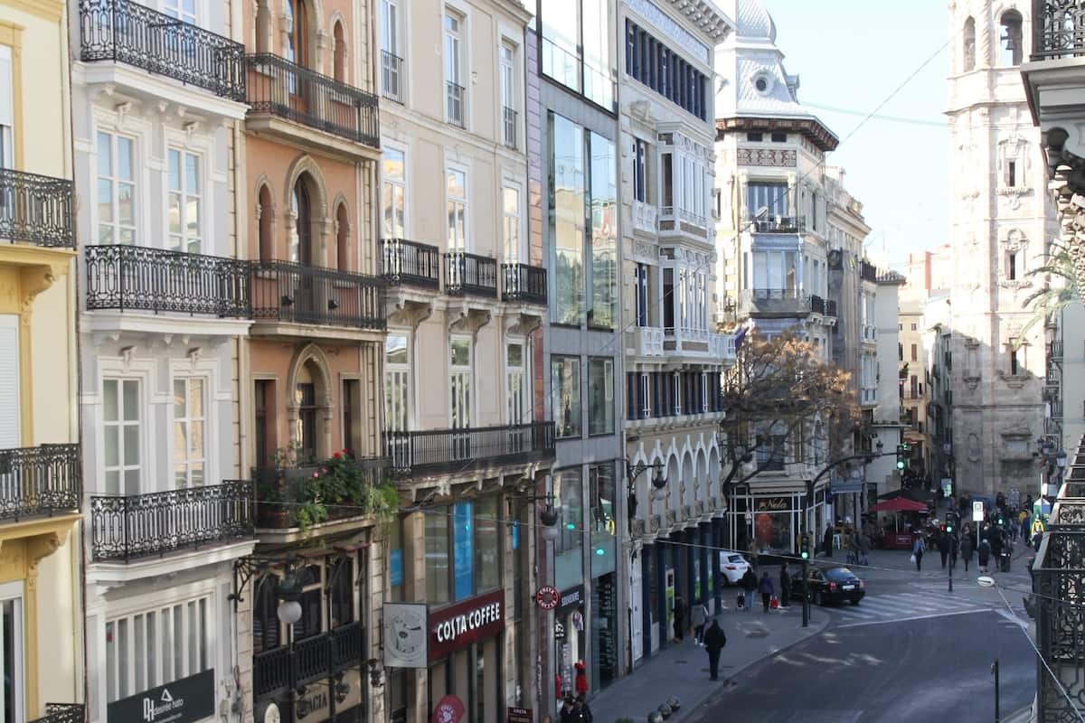 Une vue de rue avec des bâtiments, un ciel dégagé et quelques piétons.