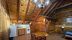 Una cabaña de madera con una zona de cocina, una mesa de comedor y una cama.