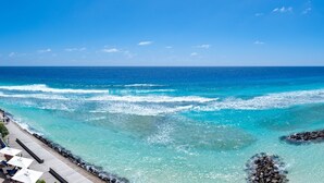 Une plage aux eaux turquoise et limpides, une digue rocheuse et une promenade en bois agrémentée de parasols.