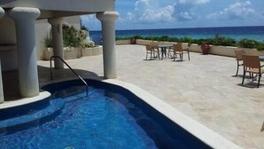 Un espace piscine extérieur avec vue sur l’océan, agrémenté de chaises et d’une table.
