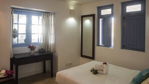 Une chambre d’hôtel avec un lit, un bureau agrémenté d’un vase de fleurs, un miroir et deux fenêtres avec des rideaux.