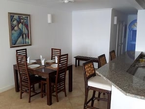 A dining area with a wooden table and chairs, a painting on the wall, and a kitchen area with a granite countertop.