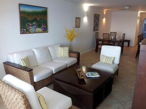 A living room with a sectional sofa, a coffee table, and a dining area with wooden chairs and a table.