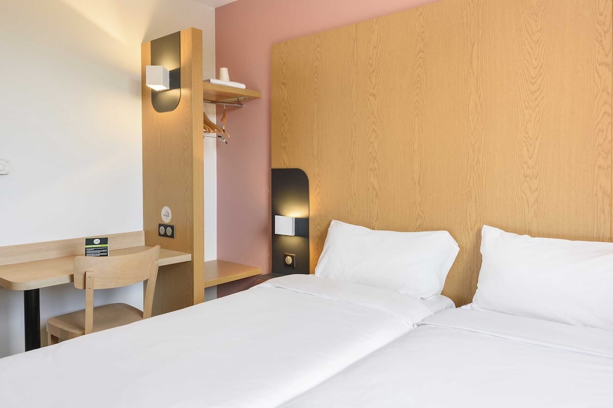 Ett hotellrum med en sänggavel i trä, ett skrivbord med en stol och en säng med vita sängkläder.