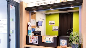 Un mostrador de recepción con un cartel que dice "Bienvenue chez B&B Hotels", una pantalla y carteles informativos.