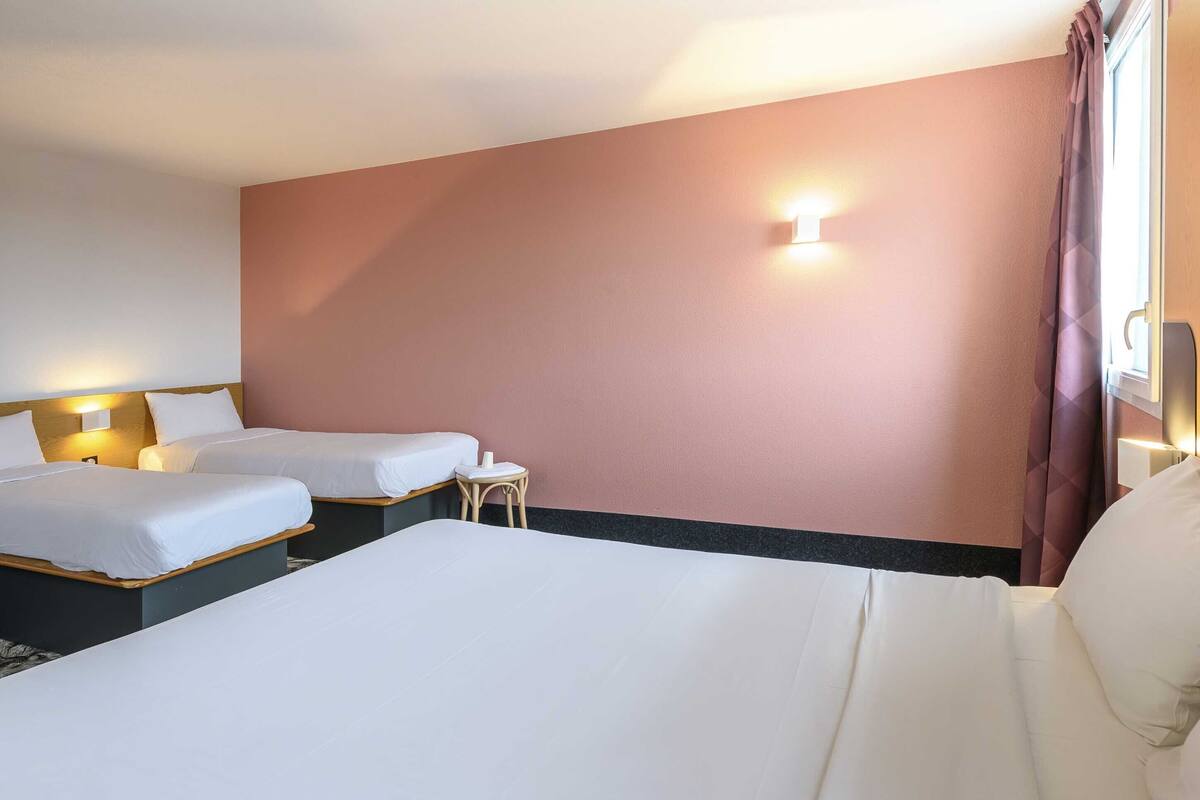Ett hotellrum med två sängar, ett litet bord och en väggmonterad lampa.