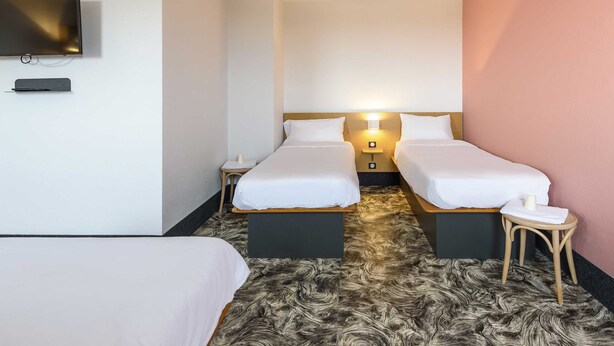 A hotel room with two beds, a TV mounted on the wall, and a small table with a lamp. - B&B HOTEL Toulouse Purpan Zénith (Toulouse)