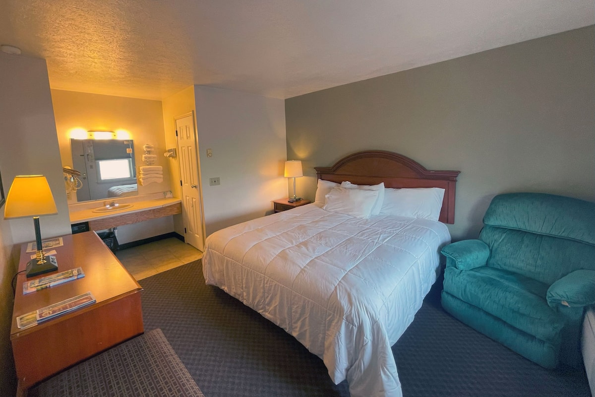Quarto de hotel com cama, escrivaninha com luminária, cadeira e espelho.