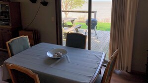 Un coin repas avec une table dressée pour quatre personnes, un saladier de fruits et une vue sur une terrasse et un espace barbecue extérieur.