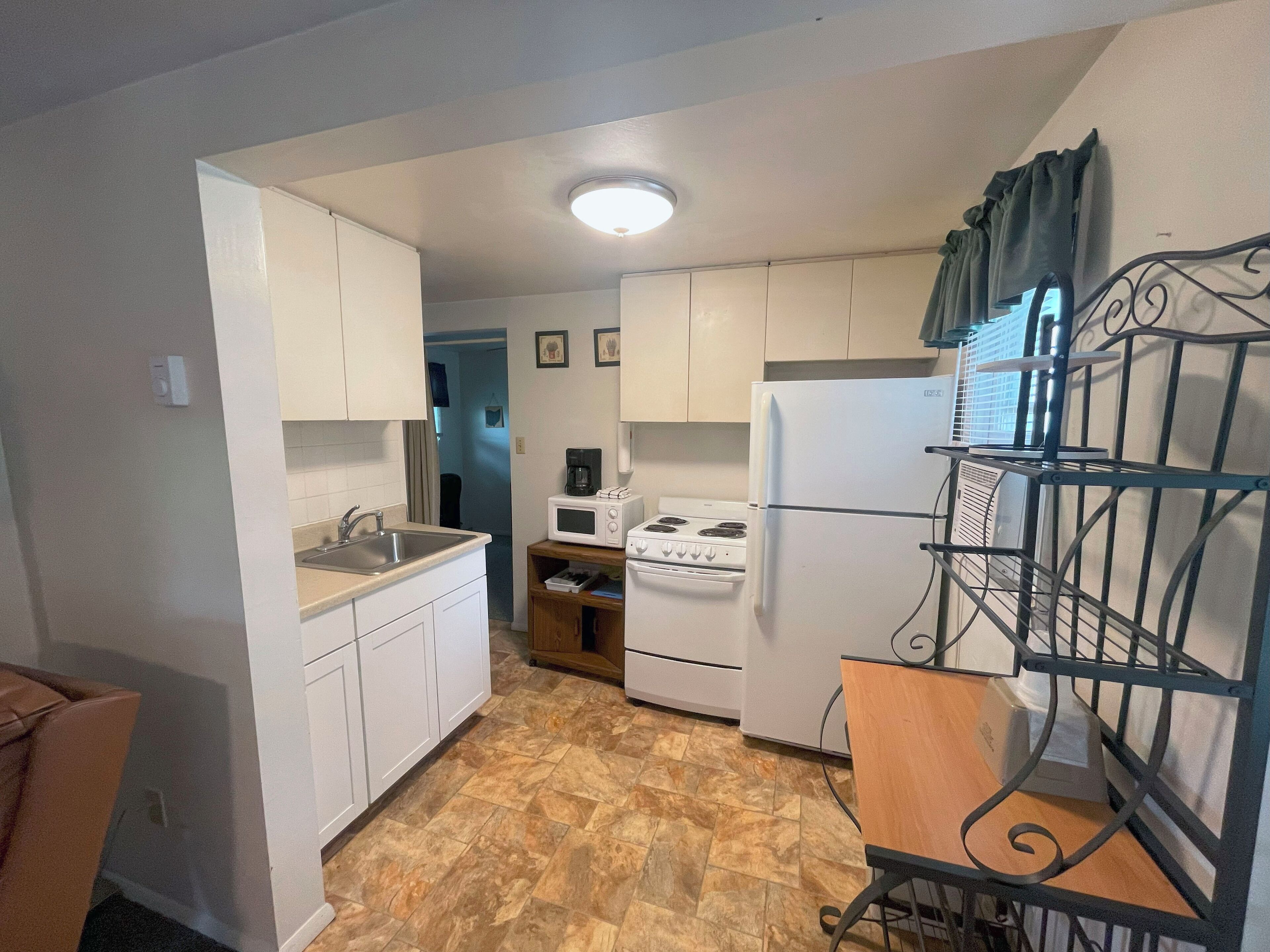 A compact kitchen with white cabinets, a stove, a microwave, and a refrigerator.