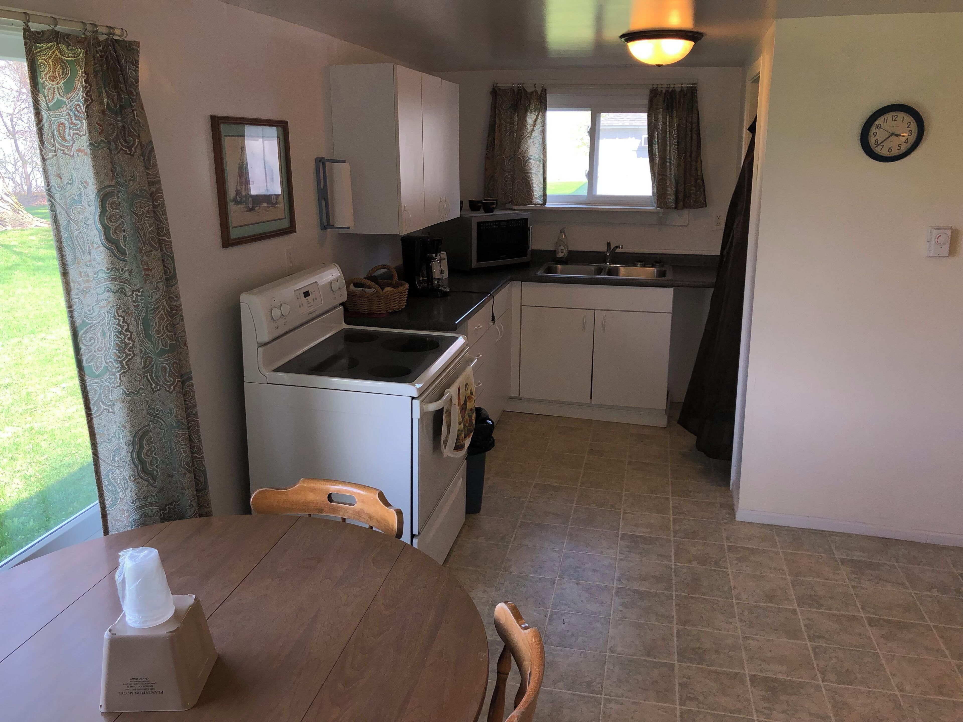 A compact kitchen with a stove, microwave, and sink. There is a dining table with chairs and a basket on the counter.