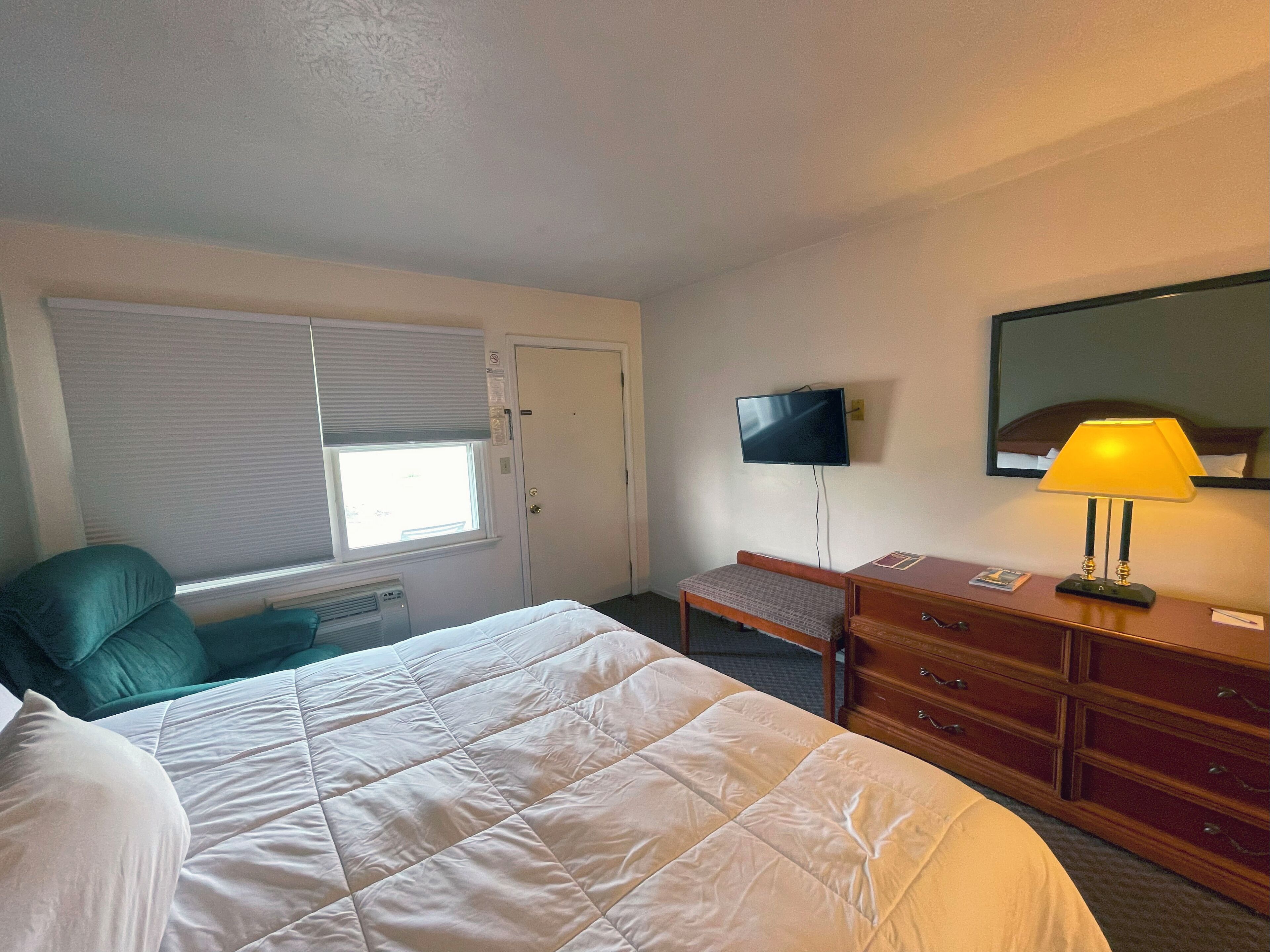 Una camera d'albergo con un letto, una scrivania, una sedia, una televisione e un comò.