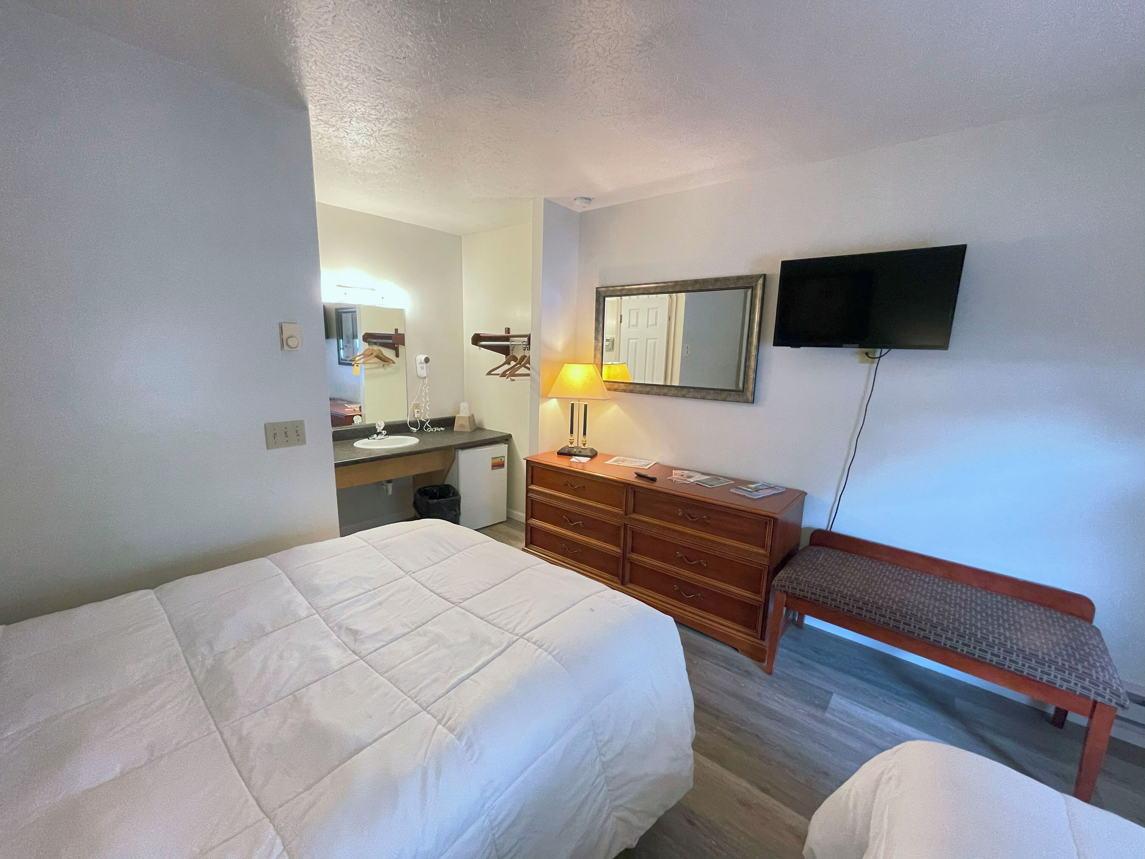 Une chambre d’hôtel avec un lit, une commode, un miroir, une télévision et un banc.