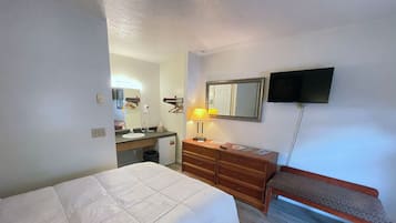 Une chambre d’hôtel avec un lit, une commode, un miroir, une télévision et un banc.
