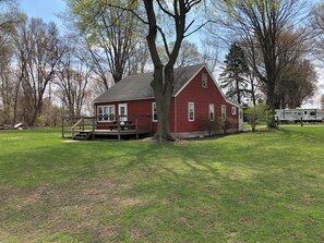 A red house with a porch and a picnic table, surrounded by trees and grass.
