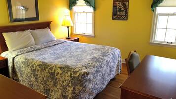 Quarto de hotel com cama, escrivaninha, luminária, janela com cortinas e detalhes decorativos nas paredes.