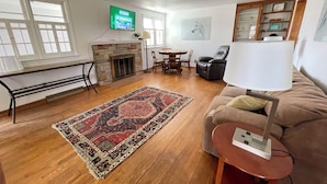 Un salon avec une cheminée, un canapé, une table basse, un téléviseur fixé au mur et un coin repas avec des chaises et une table.