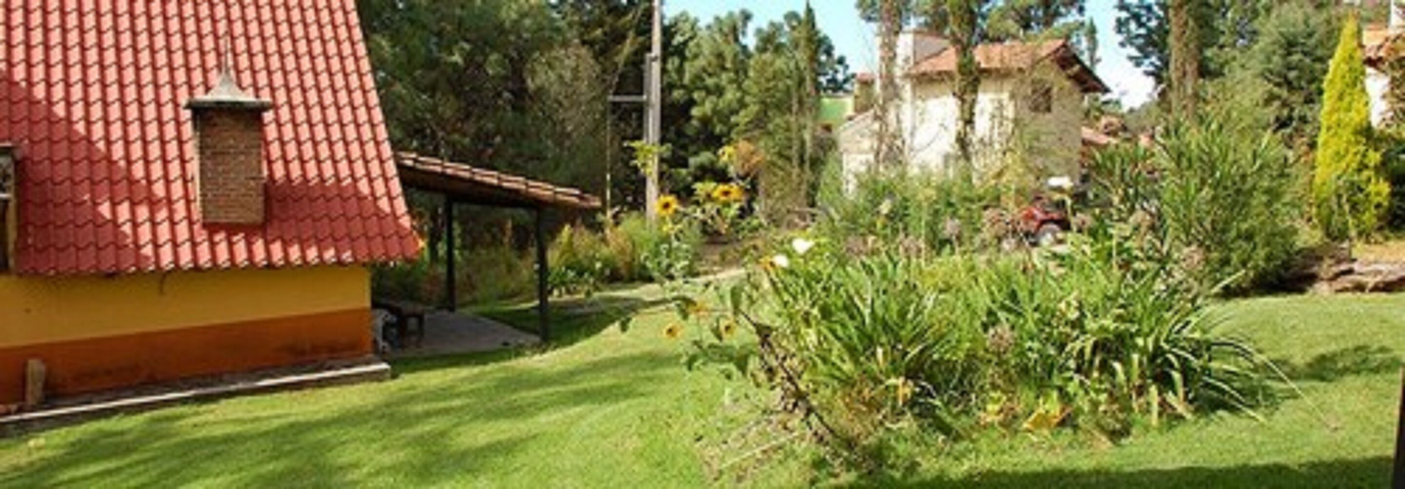 A house with a red tiled roof and a yellow facade, surrounded by a well-maintained garden with various plants and a lawn.