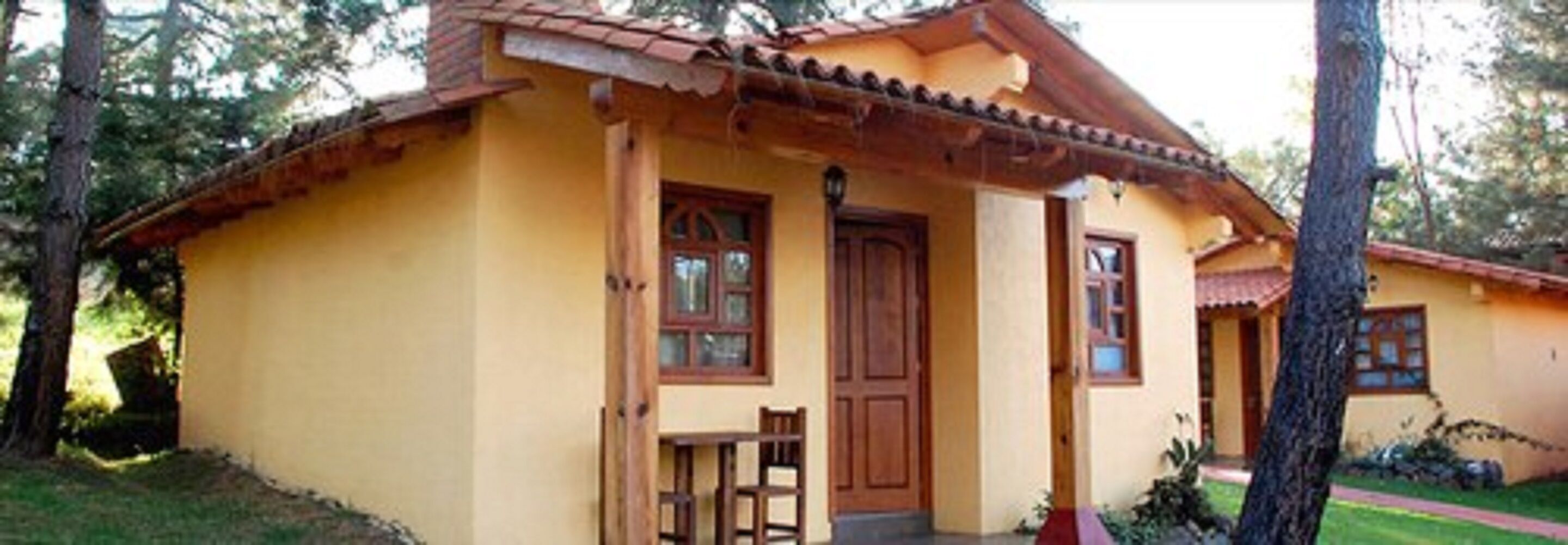 A yellow building with a tiled roof, a wooden door, and a small porch with a bench.