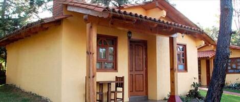 A yellow building with a tiled roof, a wooden door, and a small porch with a bench.
