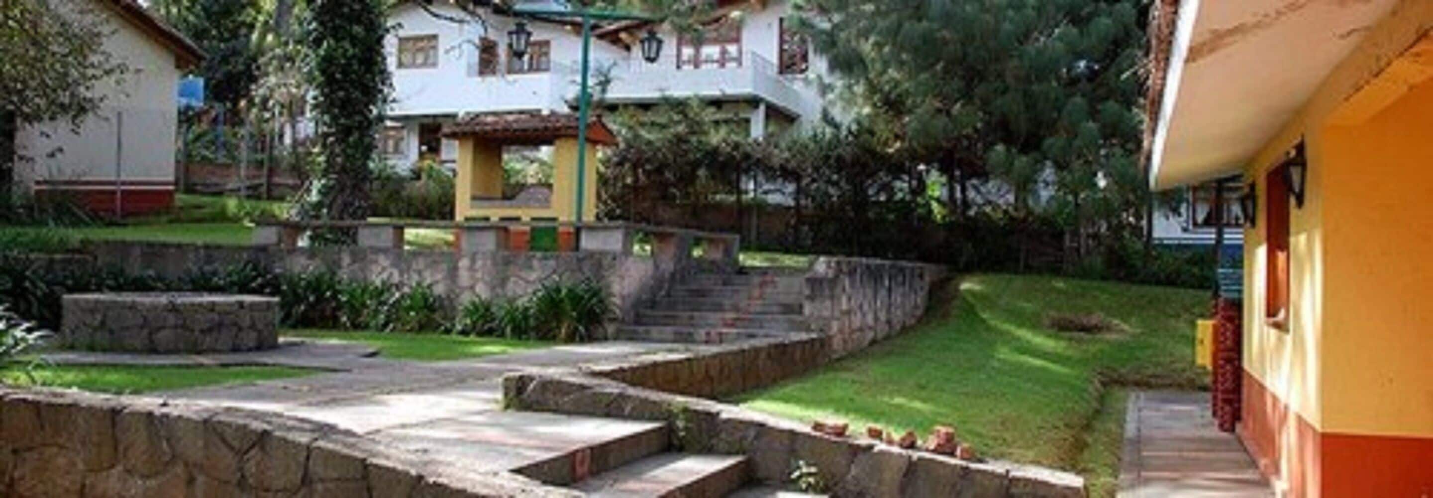 Un patio con escalones de piedra que conducen a la entrada de un edificio, rodeado de vegetación y un muro de piedra.