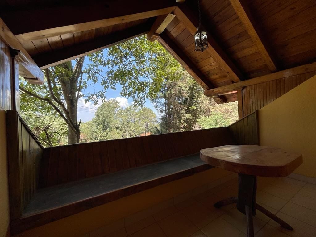 A wooden ceiling with a skylight, a bench, and a table in a room with a view of trees.