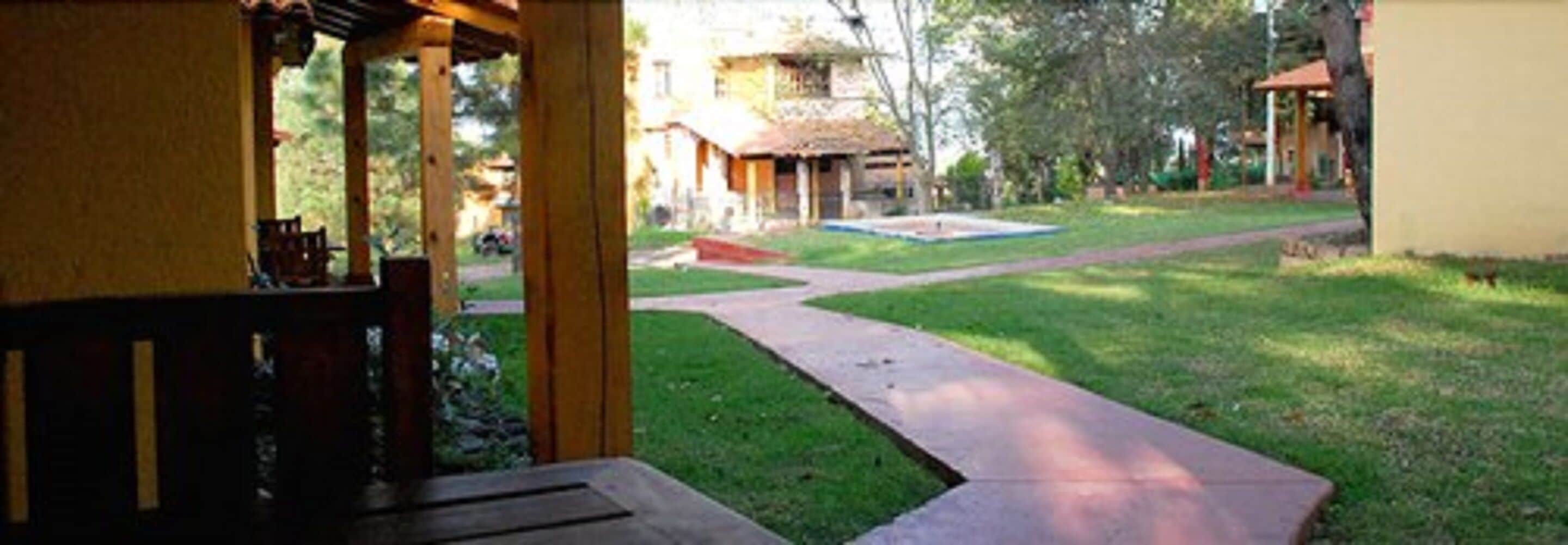 A covered outdoor seating area with a concrete path leading to a building with a thatched roof.
