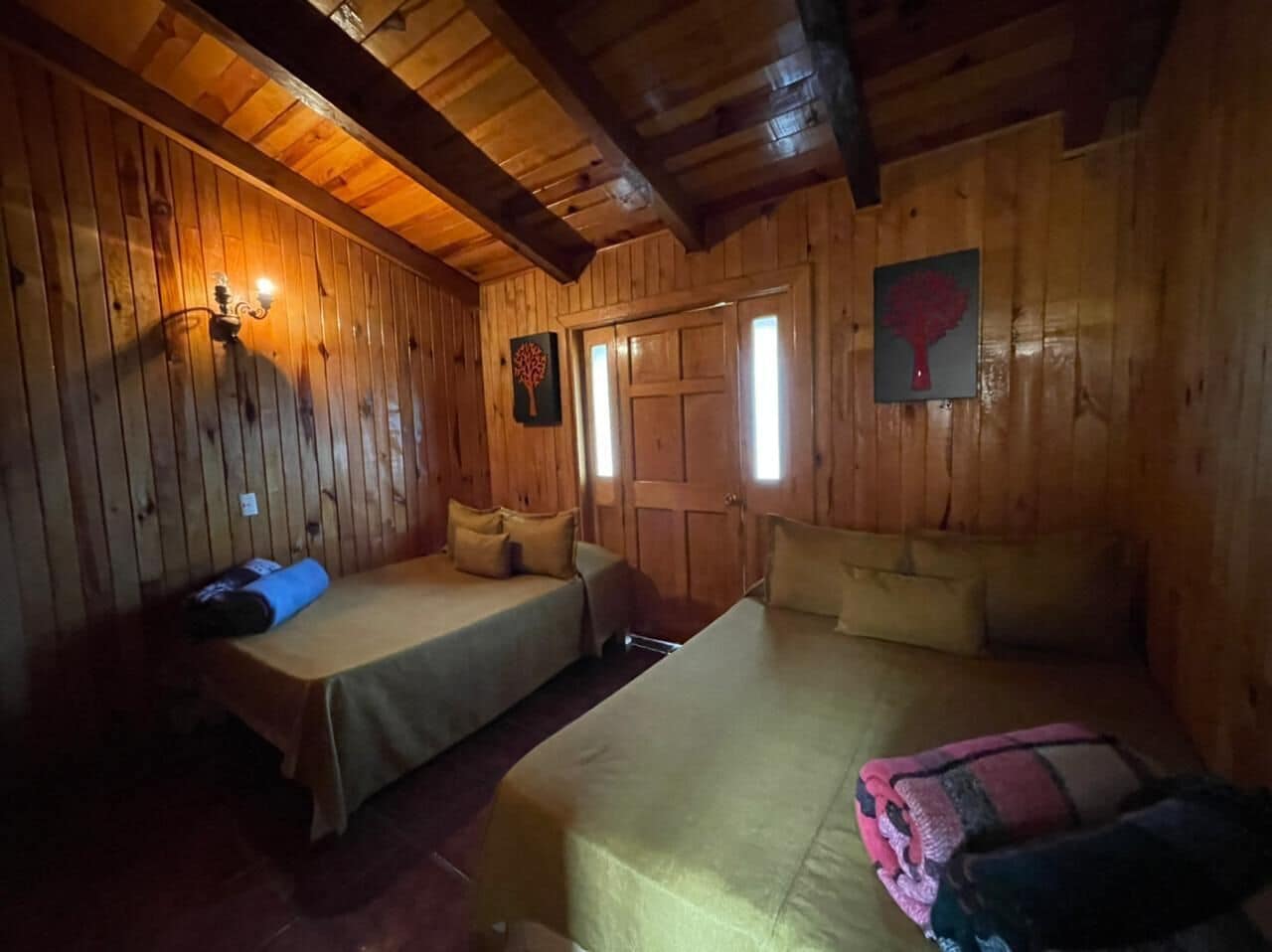 A wooden cabin room with two beds, a wooden ceiling, and a door with windows.