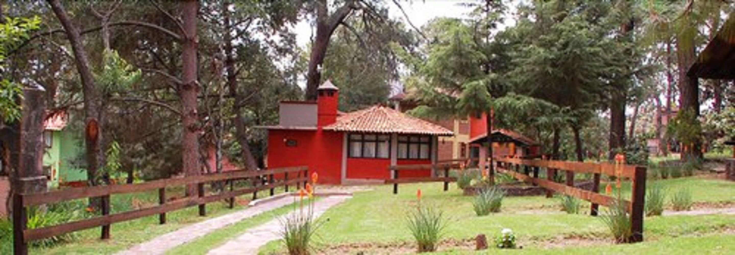 Un edificio rojo con tejado de tejas, rodeado por una valla de madera y follaje.