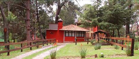 Un edificio rojo con tejado de tejas, rodeado por una valla de madera y follaje.