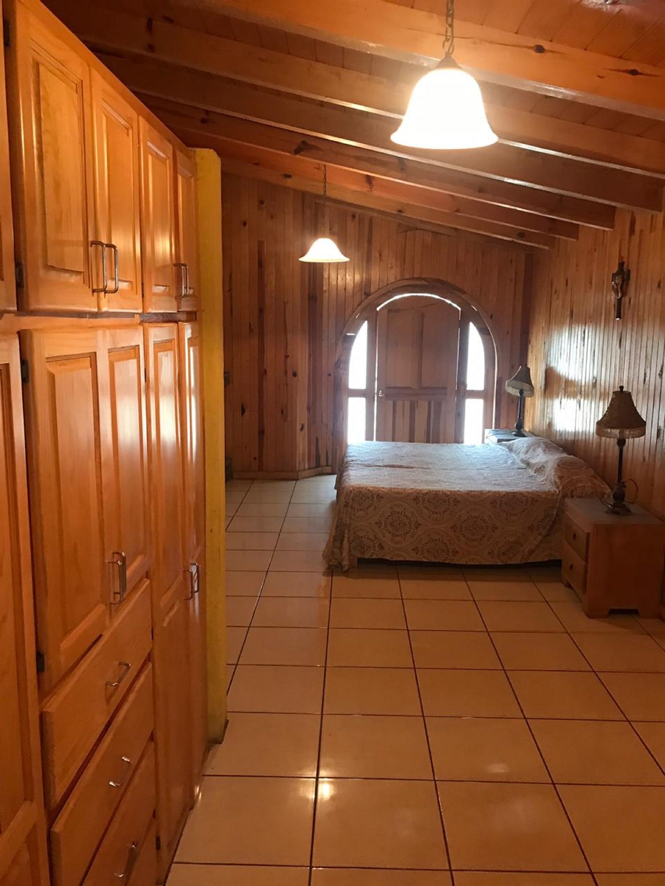 A bedroom with wooden walls, a bed, a nightstand, and a window with a view.