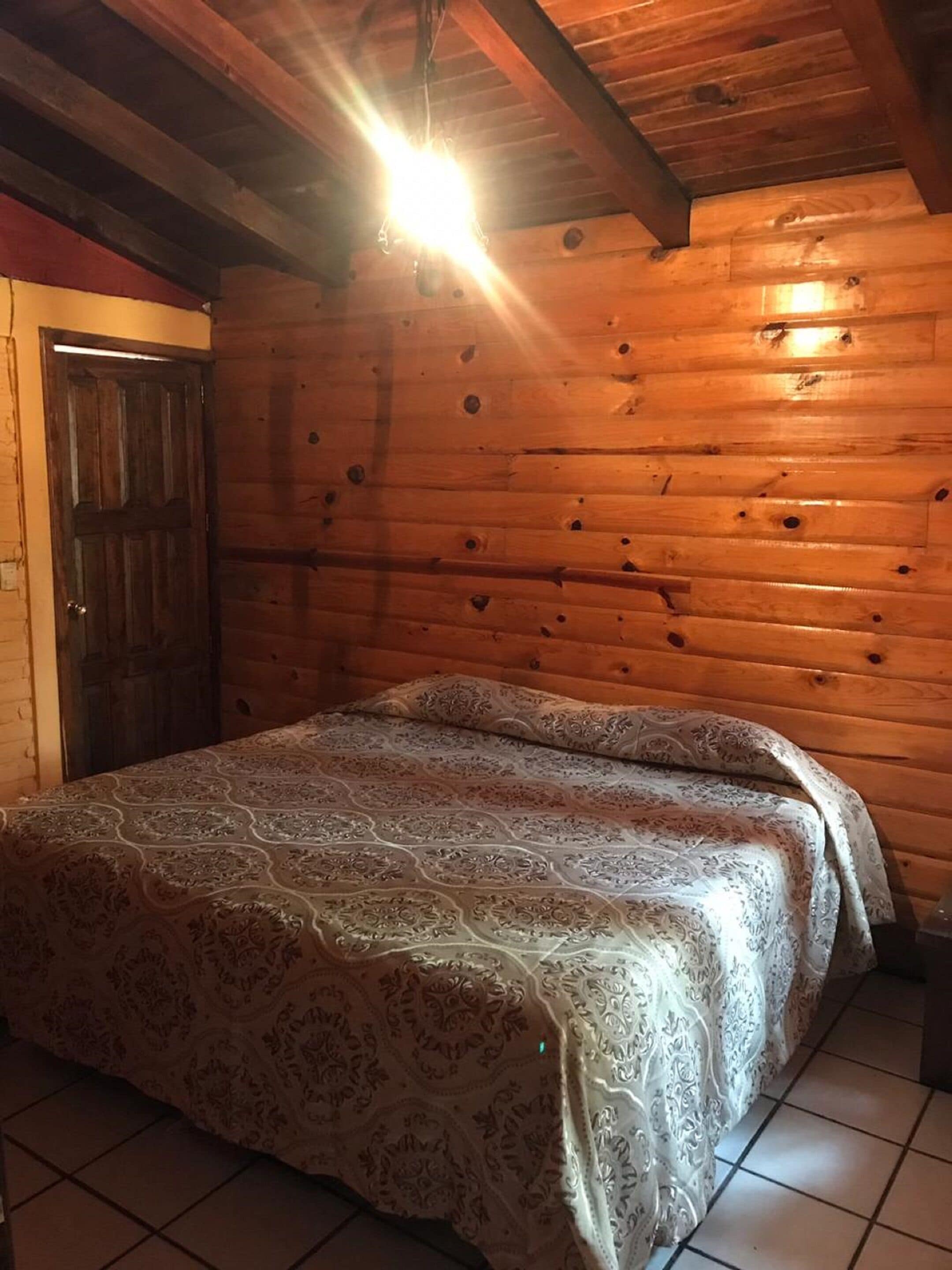 Une pièce de cabane en bois comprenant un lit, une porte et un luminaire suspendu.