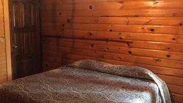 Une pièce de cabane en bois comprenant un lit, une porte et un luminaire suspendu.