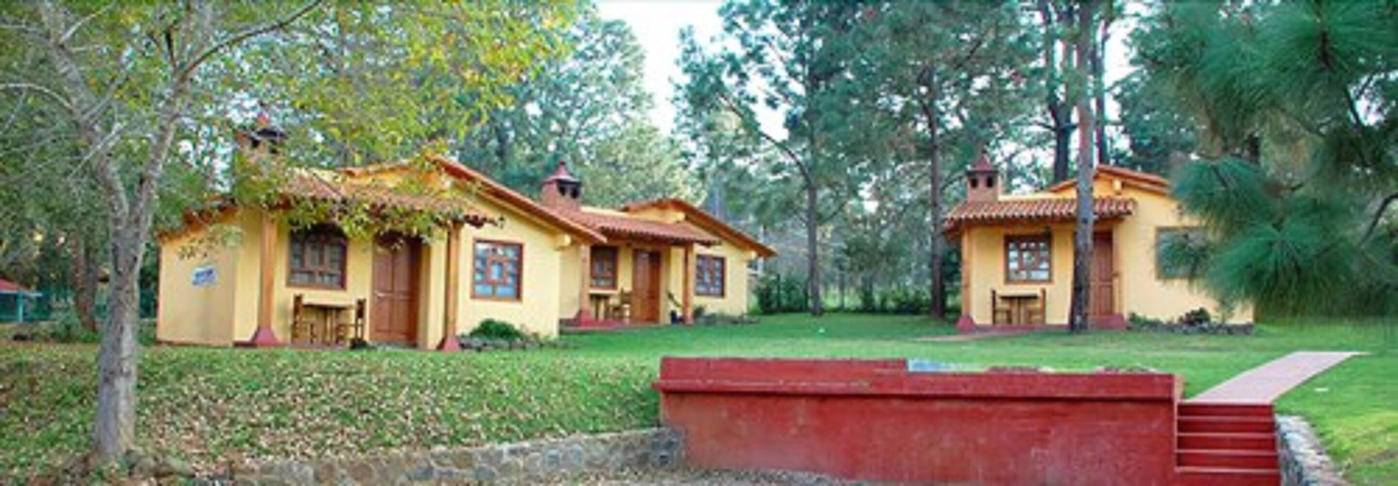 A yellow building with a tiled roof, surrounded by trees and a grassy area.