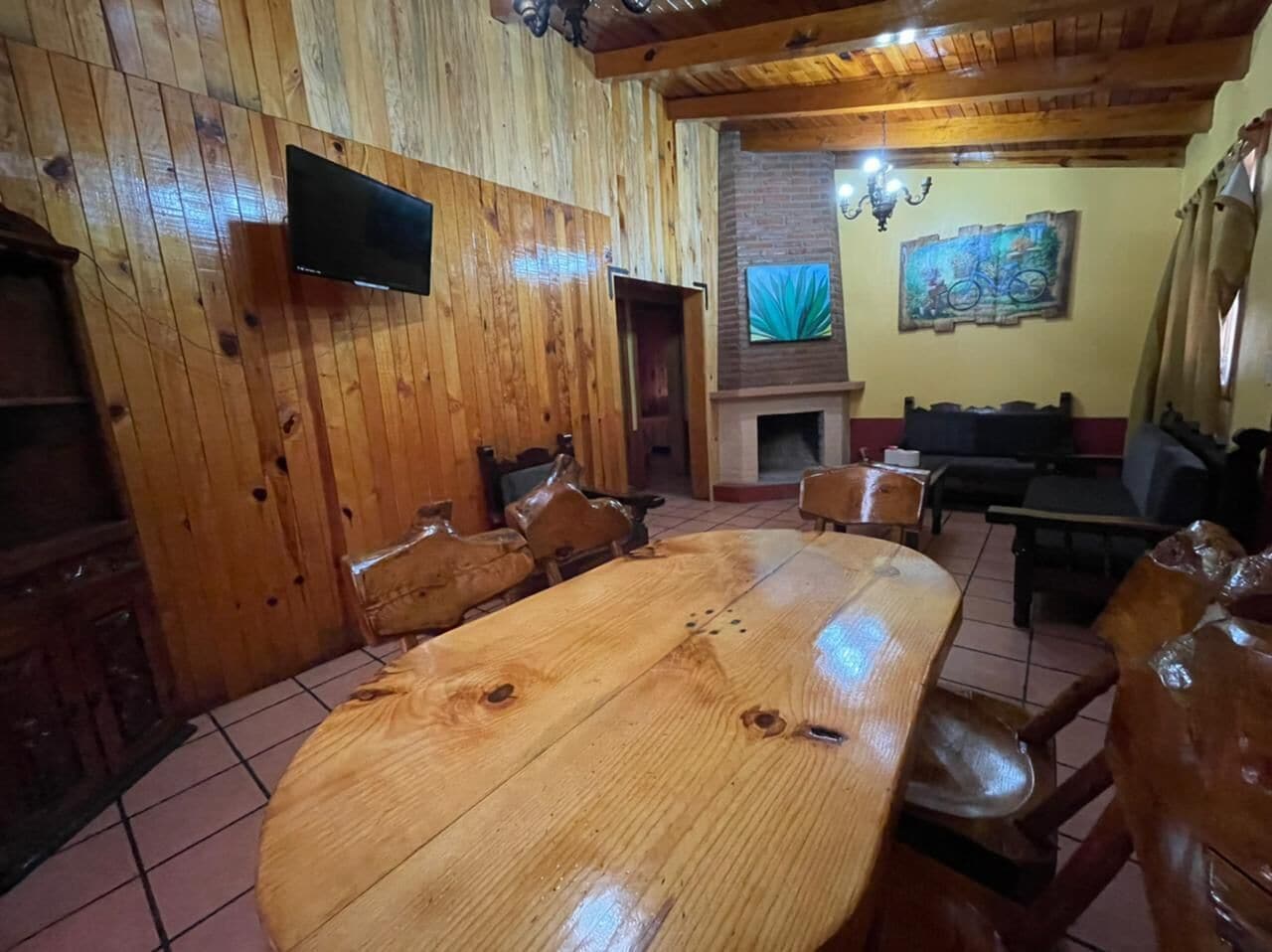 A wooden-paneled room with a large wooden table and chairs, a television mounted on the wall, and a fireplace.