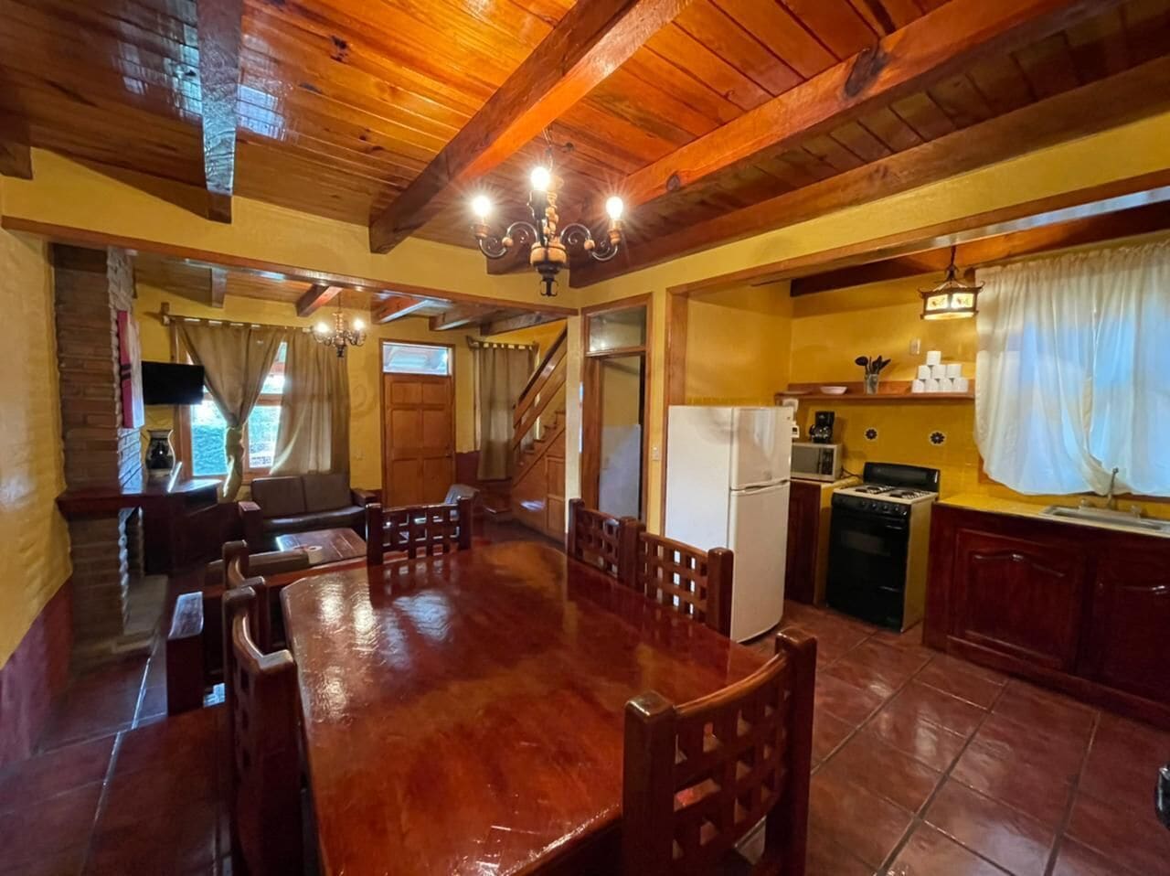 Un comedor amplio con una mesa y sillas de madera, una cocina con estufa y refrigerador, y una escalera que conduce a otro nivel.
