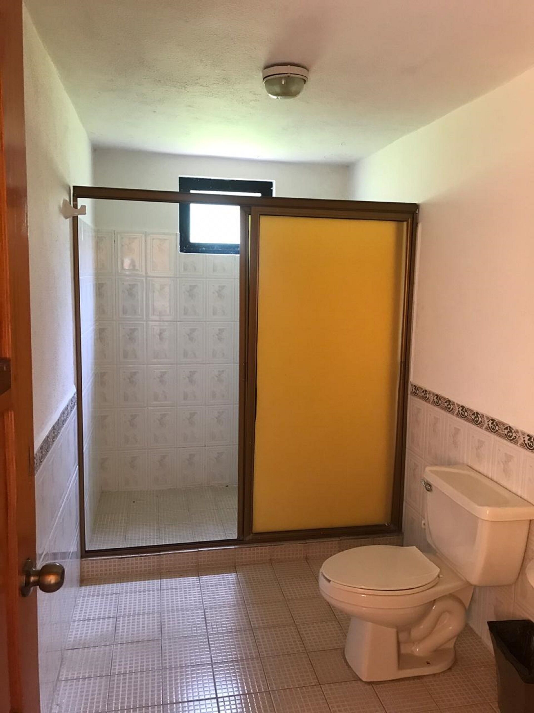 Un baño con inodoro, cabina de ducha y suelo de baldosas.