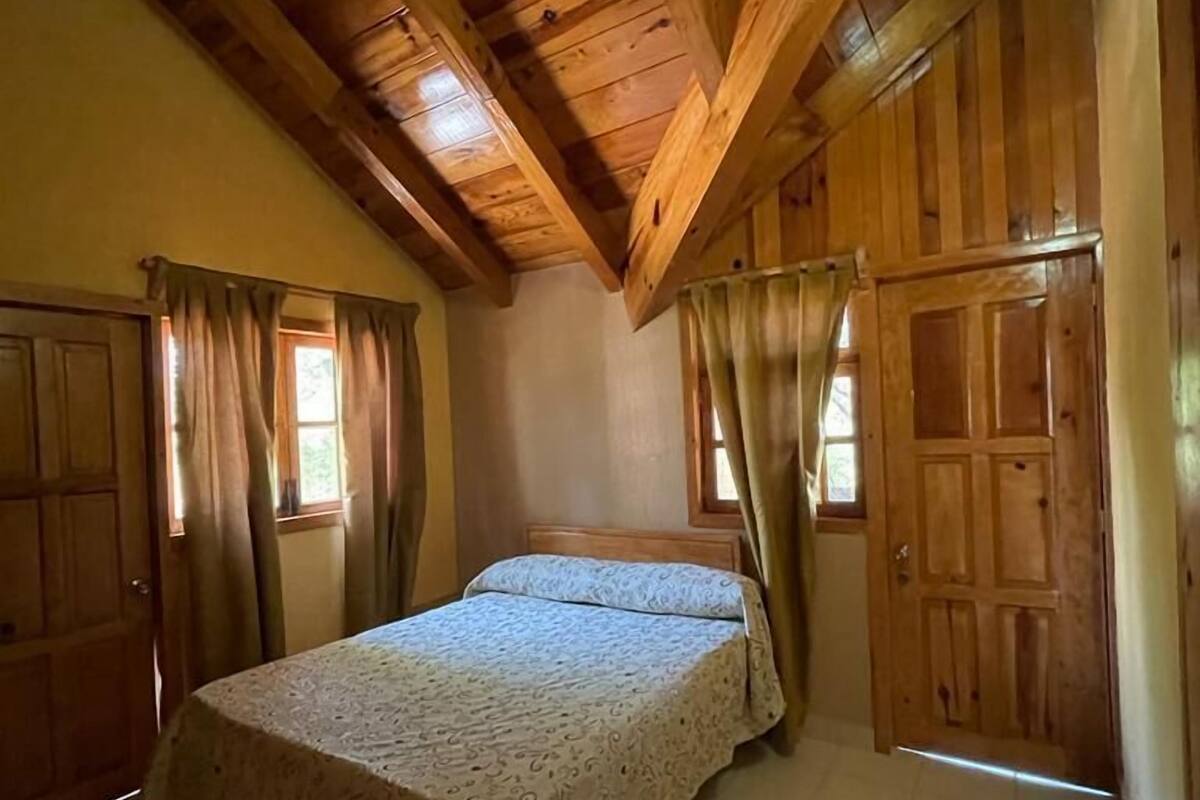 A bedroom with a wooden ceiling, a bed with a patterned bedspread, and two doors.