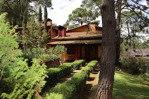 Una casa rústica con techo de tejas, rodeada de exuberante vegetación y un sendero de jardín cuidado.