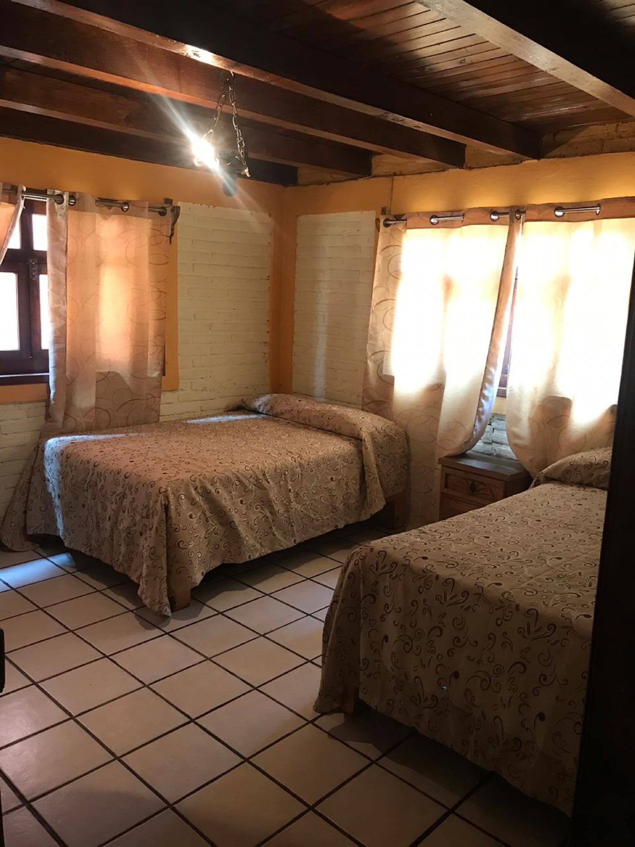 Una habitación con dos camas, vigas de madera en el techo y cortinas en las ventanas.