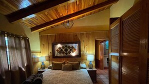 Un dormitorio con una cama grande, vigas de madera en el techo, un televisor montado en la pared y un armario de madera.