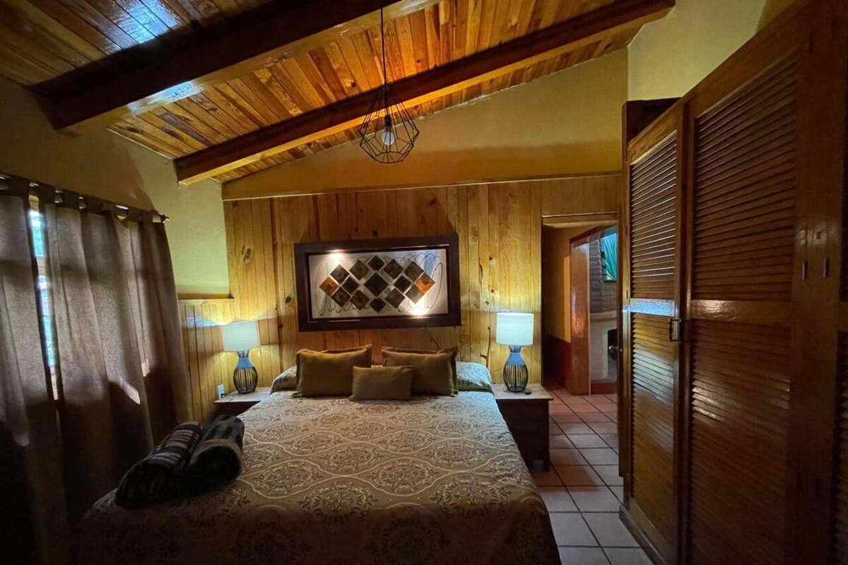 A bedroom with a large bed, wooden ceiling beams, a wall-mounted TV, and a wooden wardrobe.