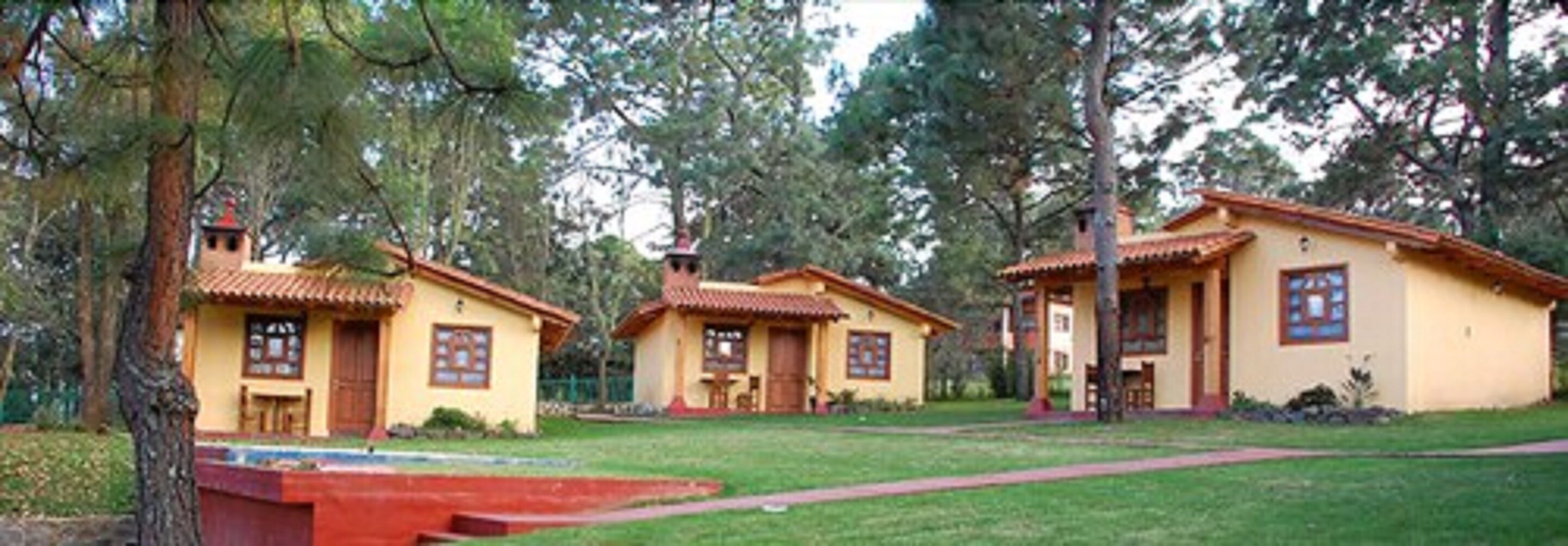 A row of yellow buildings with red roofs, surrounded by trees and a well-maintained lawn.