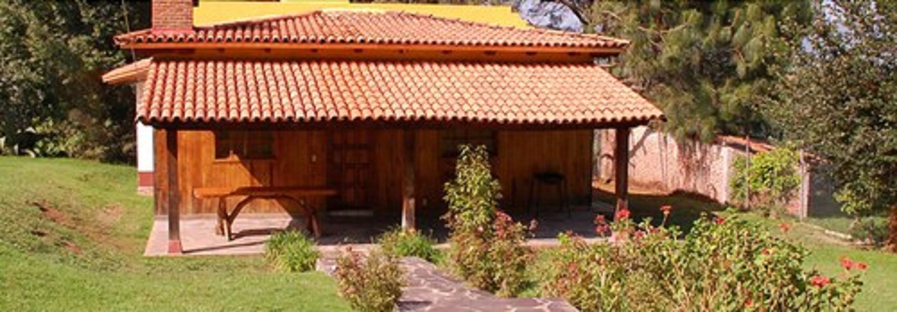 Una casa tradicional de madera con techo de tejas, un porche y un jardín con flores rojas.