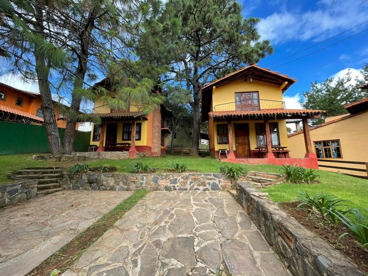 A courtyard with stone pathways and two yellow buildings with red accents, surrounded by trees.